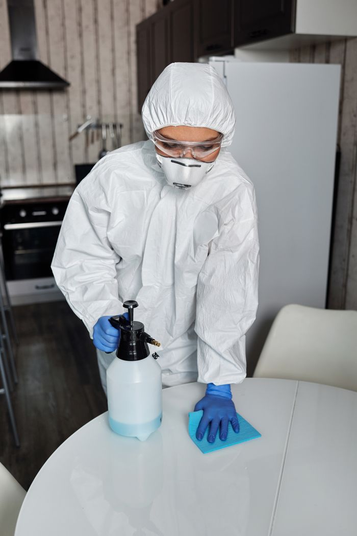 Une personne entièrement équipée en EPI désinfecte une table à l’intérieur pour l’hygiène et la sécurité.